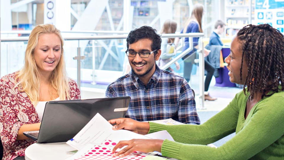 three people sitting around a table, one has a laptop